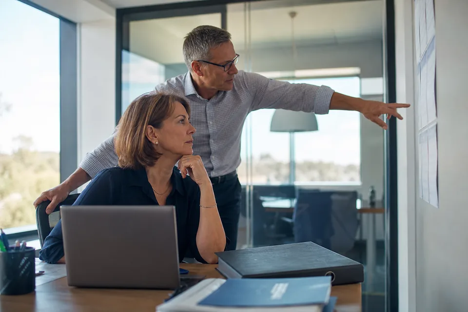 Compliance manager and a finance controller reviewing contract obligations at a desk beside a binder