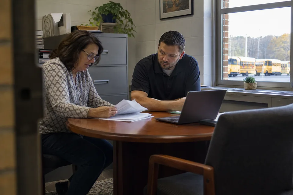 School district business manager and a purchasing coordinator reviewing vendor agreements at a table in the district office