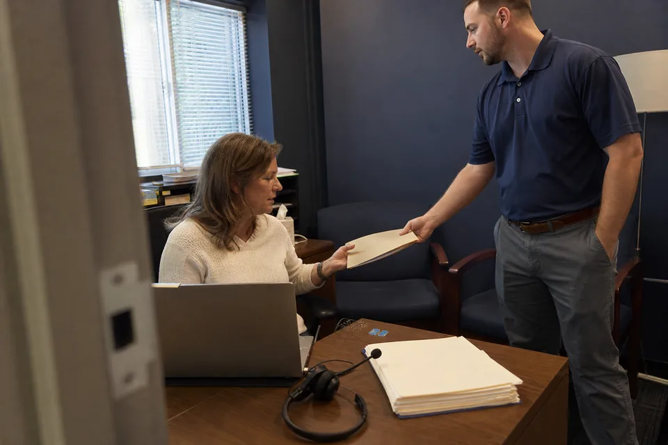 Staffing agency operations manager and a recruiter going through a folder of client agreements at a desk